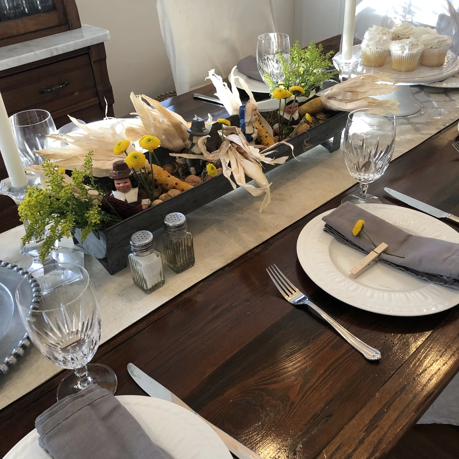 Dining table set with layered plates, glassware, flowers, and seasonal greenery