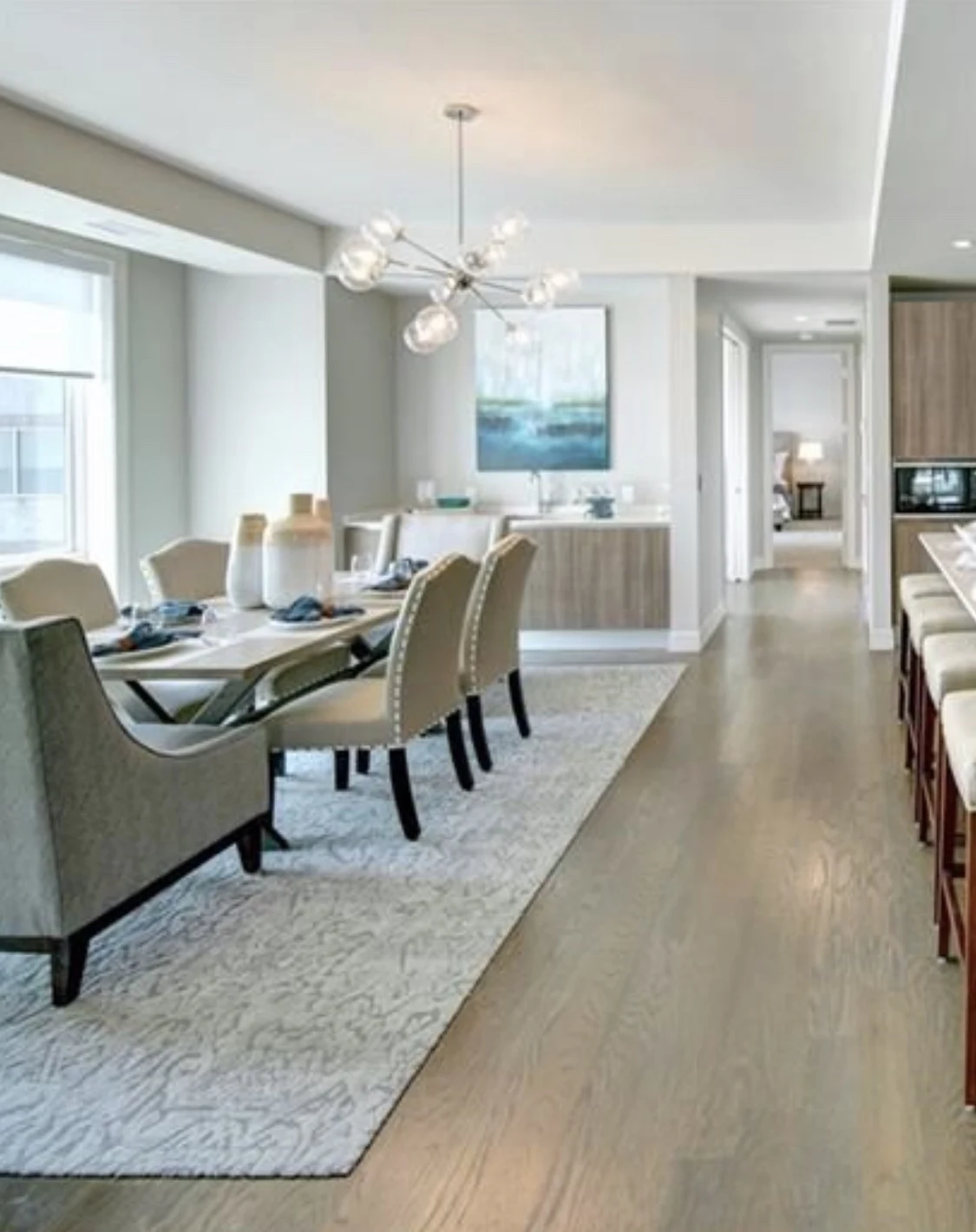 Open dining area with pale upholstered chairs, a patterned rug, and blue artwork