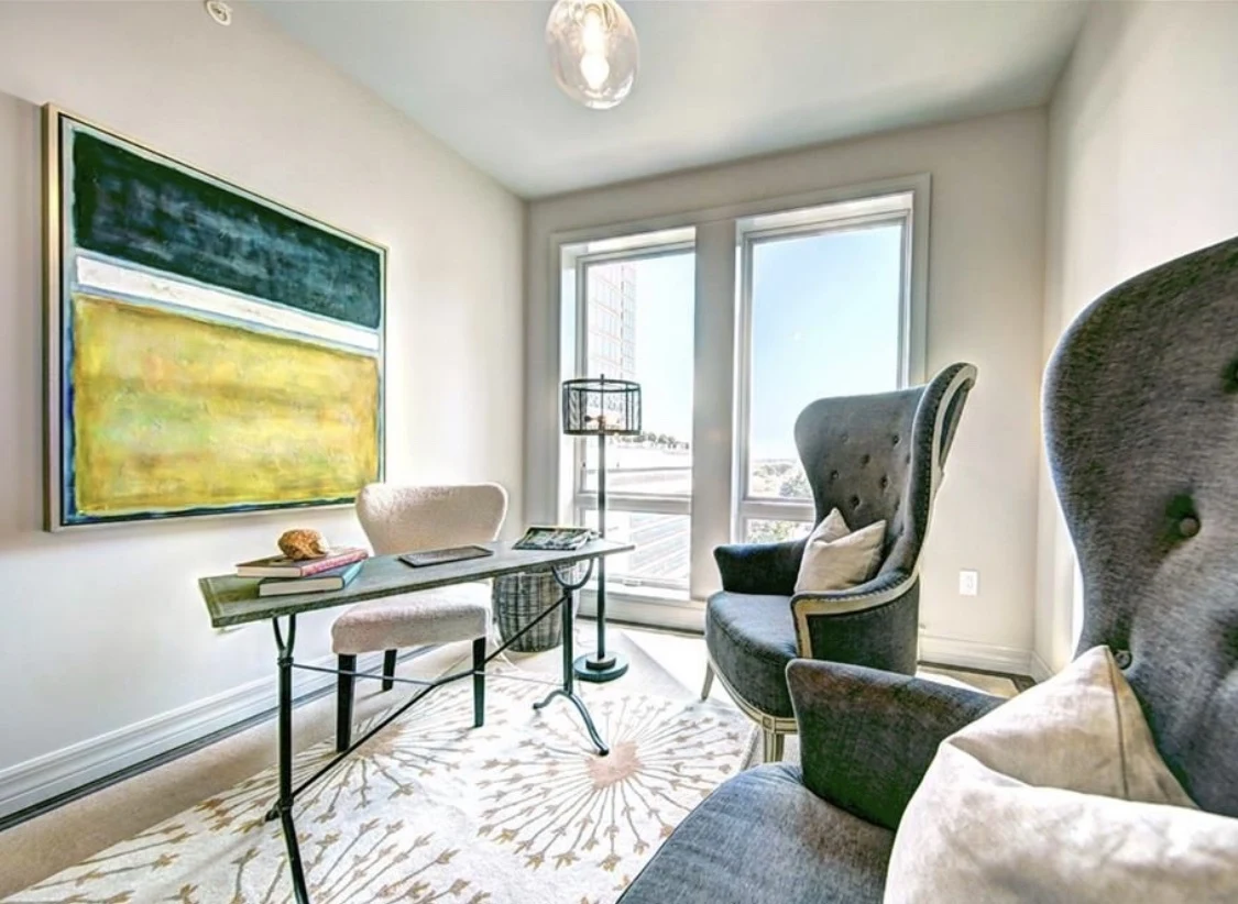 Light-filled sitting room with sculptural chairs, a glass desk, and green and yellow artwork
